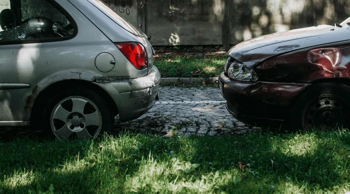 Two cars make contact on a cobblestone street; the gray car's rear touches the red car's front.